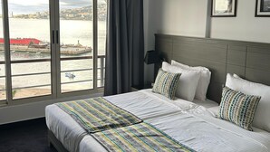 Una habitación de hotel con una cama grande, vistas al mar y al paisaje urbano.