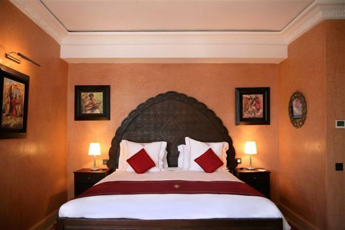 Una cama bien hecha con un cabecero oscuro, dos lámparas de noche y cuadros en las paredes.