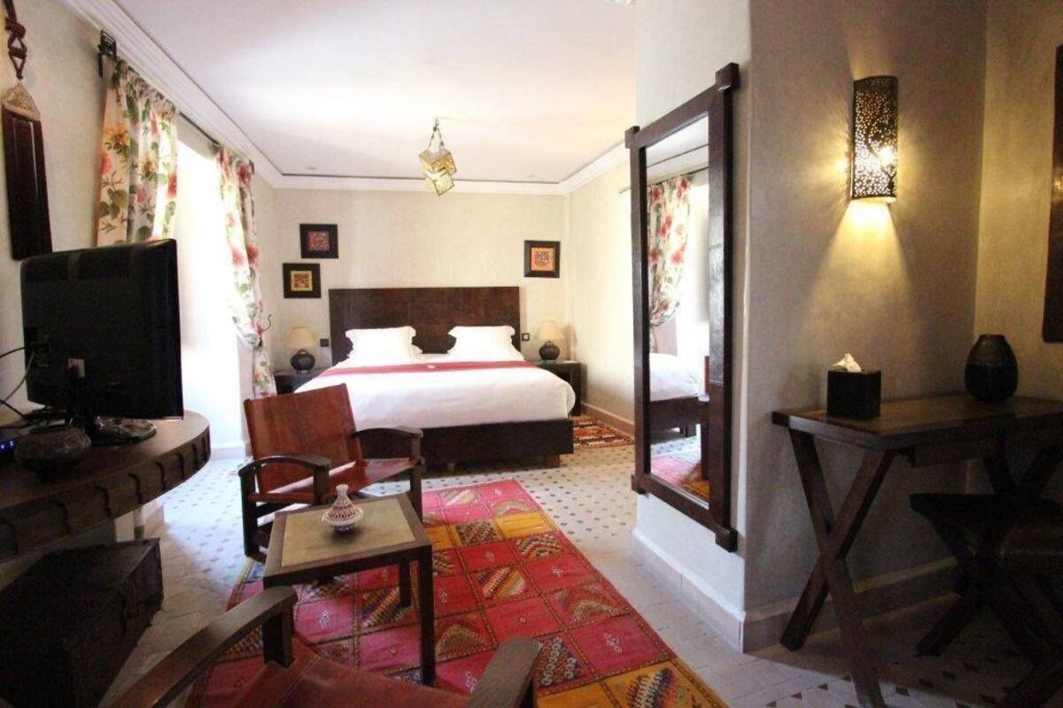 Una habitación de hotel con una cama, un escritorio, un televisor y un espejo.