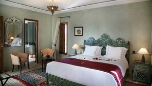 A hotel room with a large bed, a chair, a nightstand, a lamp, a mirror, and a door. - Dar Chams Tanja (Tangier)