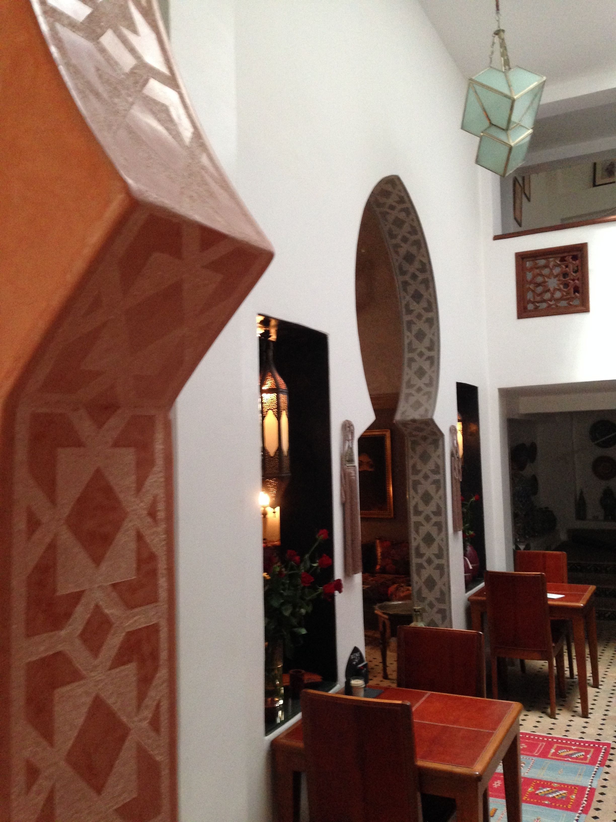 A dining area with wooden chairs and tables, a patterned wall, and a hanging light fixture.