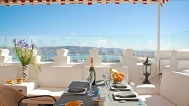 A rooftop terrace with a table set for dining, white outdoor furniture, and a view of the city and hills. - Dar Chams Tanja (Tangier)