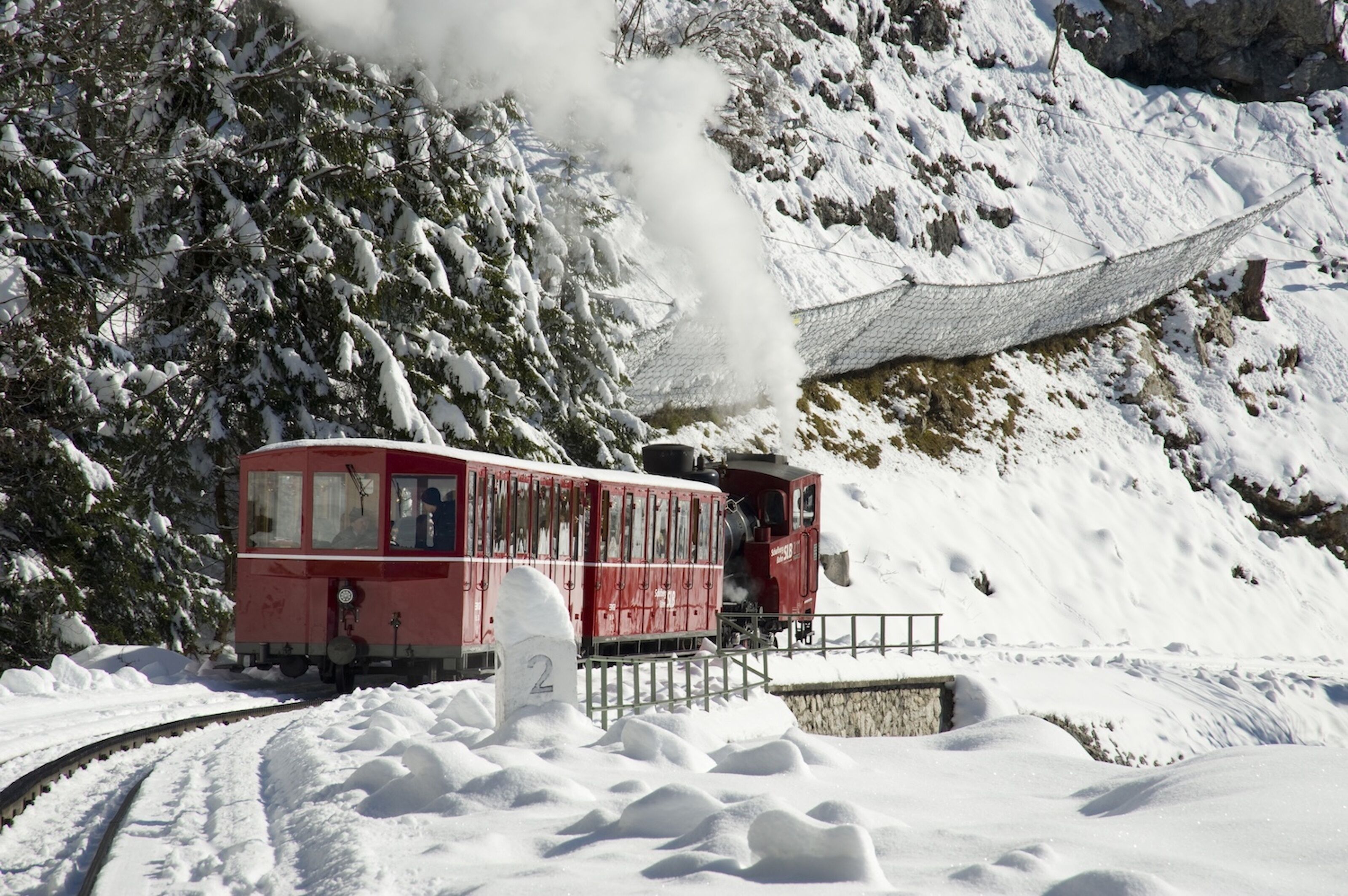 Un train rouge sur une voie ferrée enneigée, avec un panneau portant le numéro 2 au premier plan.