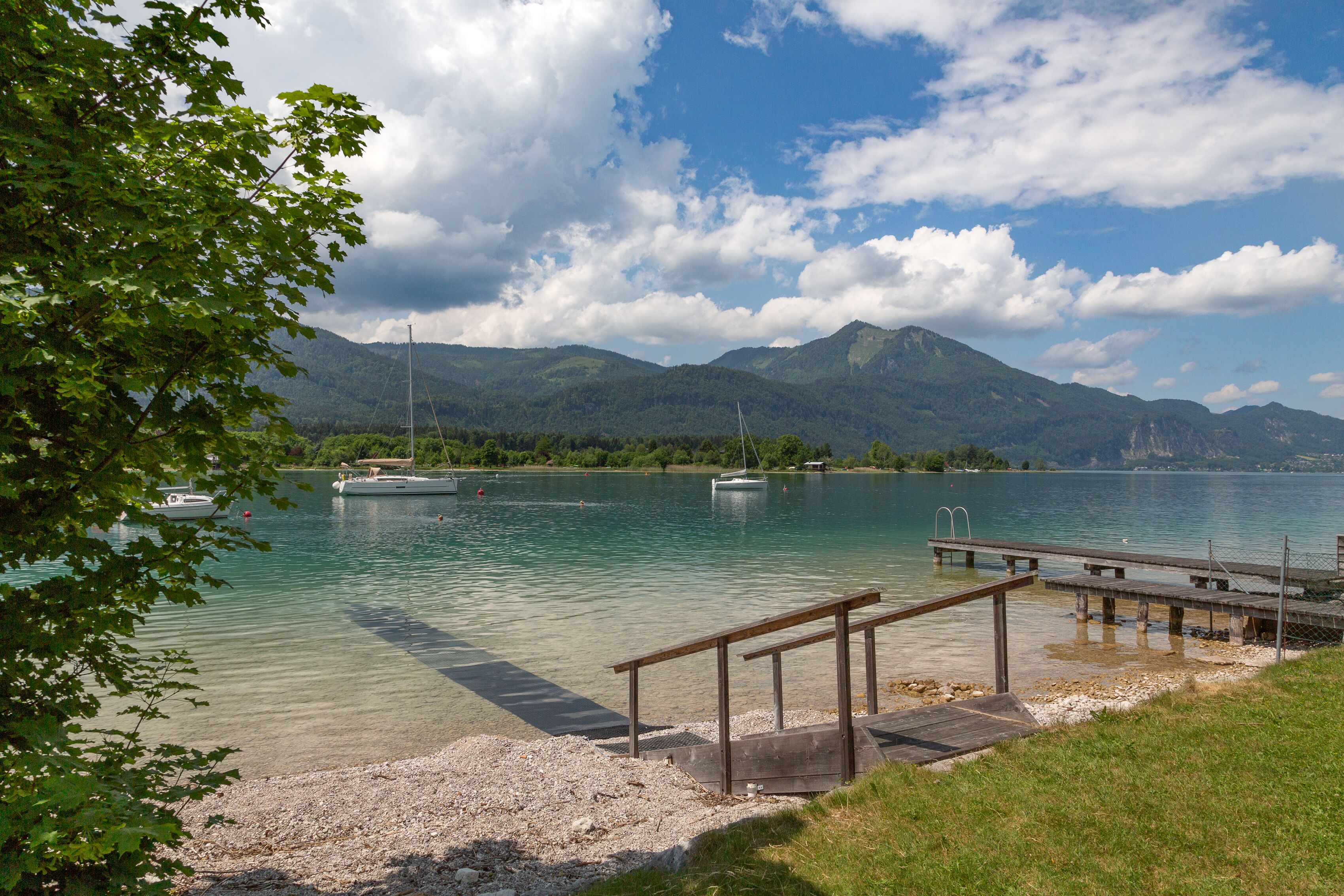 A lakeside view with boats, a wooden dock, and mountains in the background.