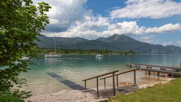 A lakeside view with boats, a wooden dock, and mountains in the background.