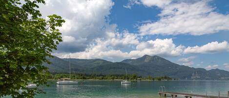 A lakeside view with boats, a wooden dock, and mountains in the background.