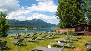 A lakeside view with lounge chairs and a wooden cabin.