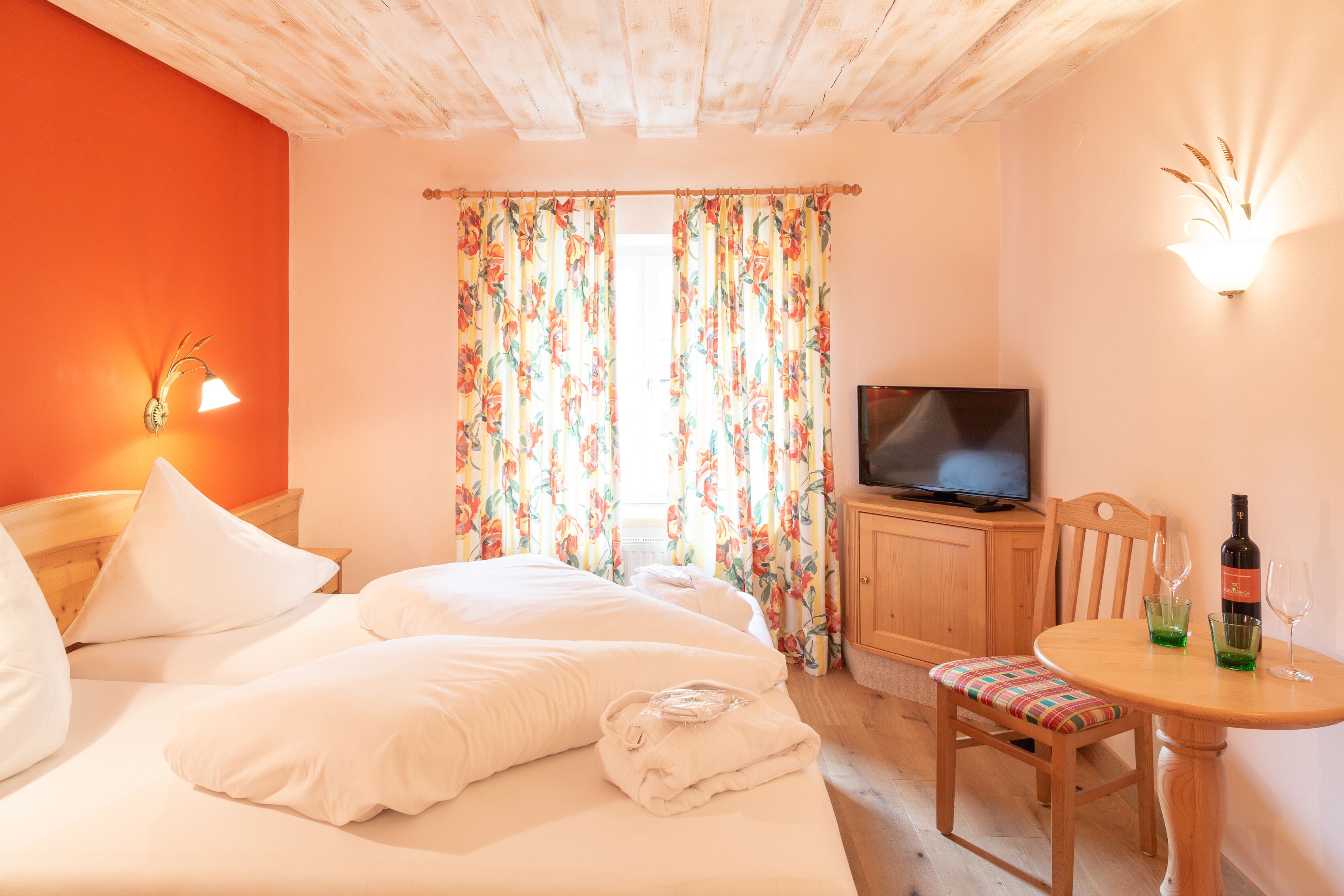 Une chambre d’hôtel avec un lit, une télévision, une table avec des verres et une bouteille, et une chaise.