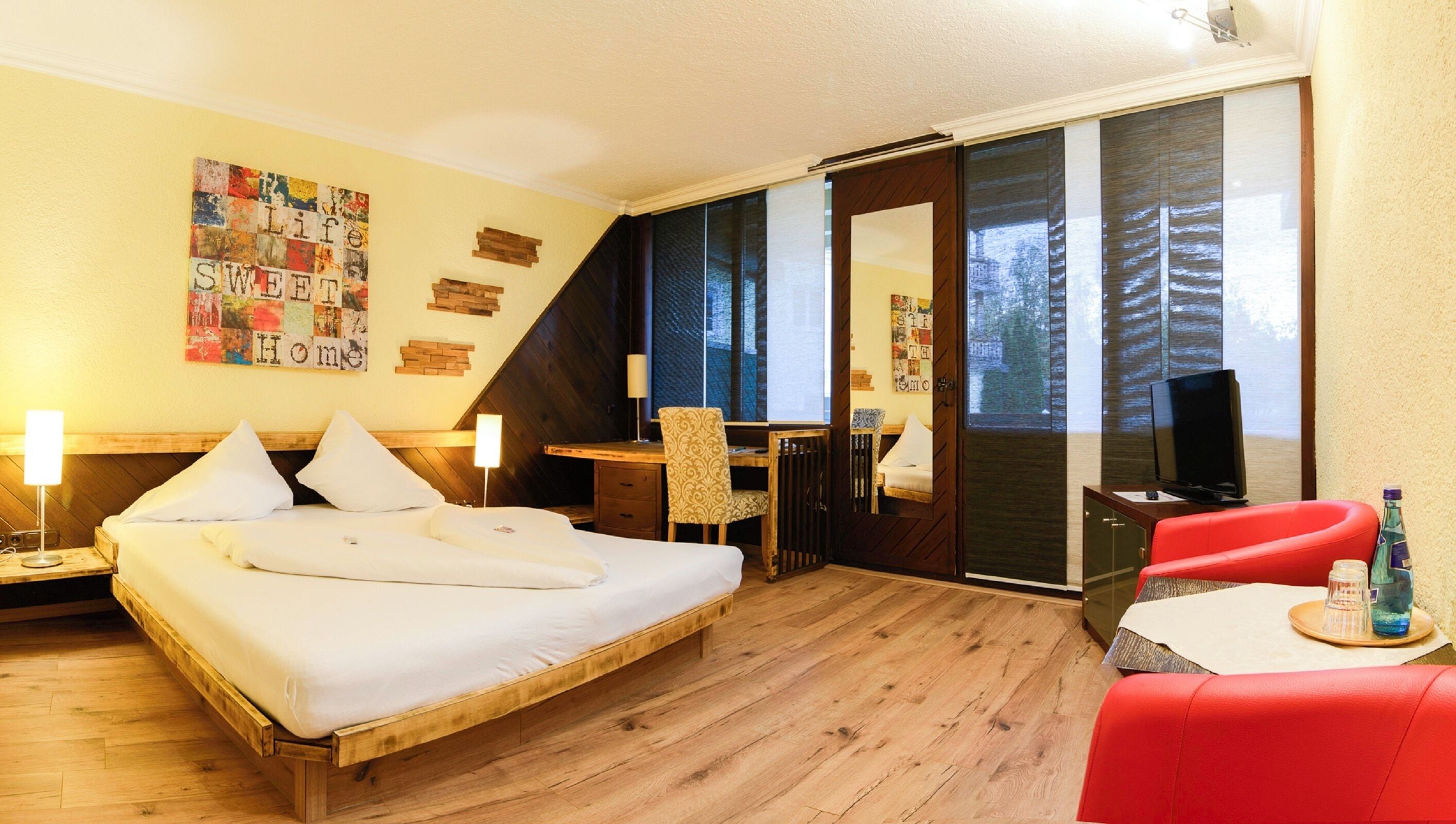 Een hotelkamer met een bed, bureau, stoel, televisie en een rode bank.