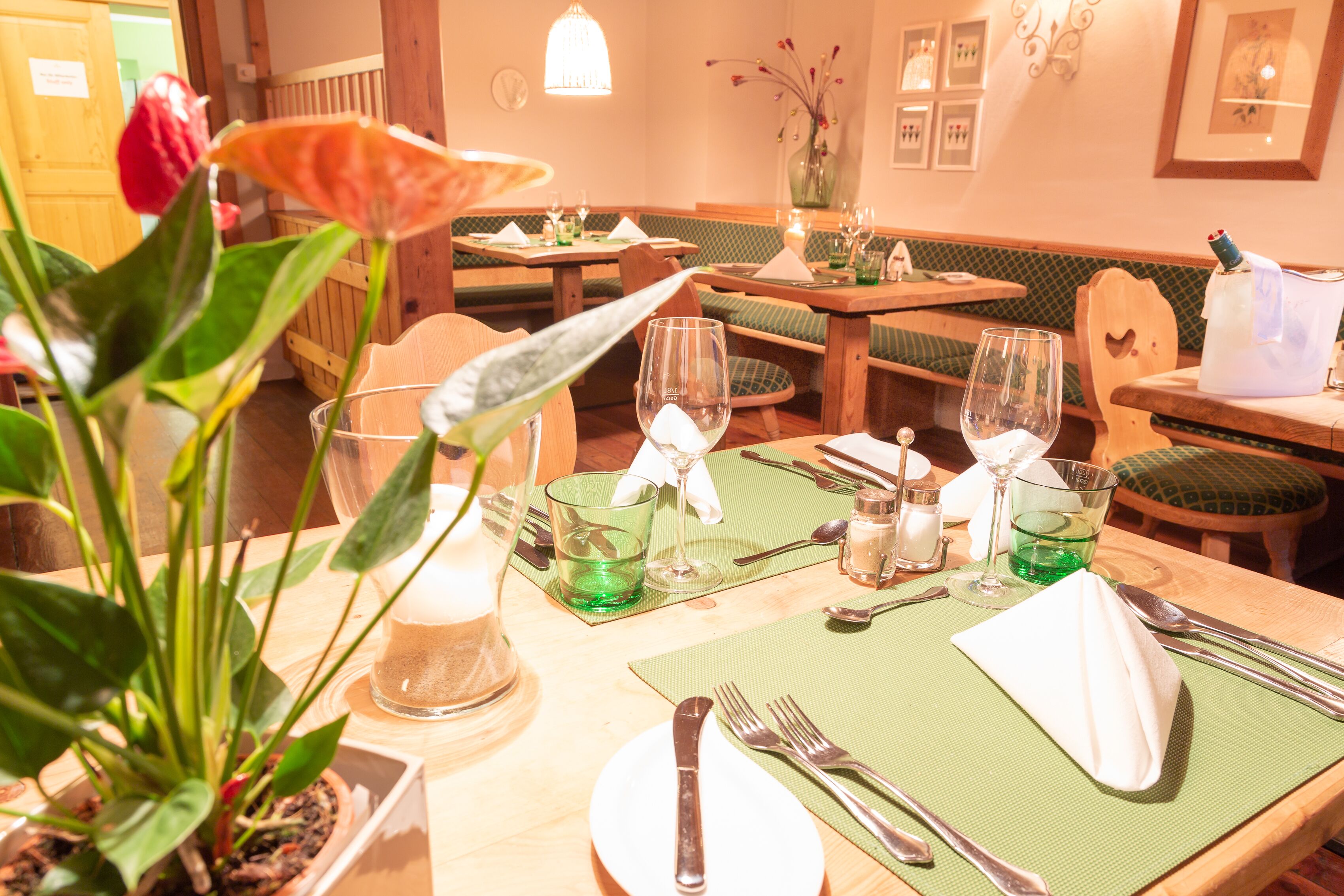 A restaurant setting with wooden tables, green cushioned booths, and a potted plant.