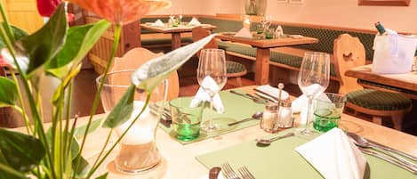 A restaurant setting with wooden tables, green cushioned booths, and a potted plant.