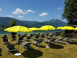 Outdoor lounge chairs and yellow umbrellas arranged on a grassy area with a lake and mountains in the background. - Hotel Försterhof (St. Gilgen)