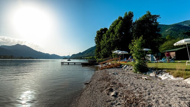 A lakeside view with a dock, umbrellas, and a small building.