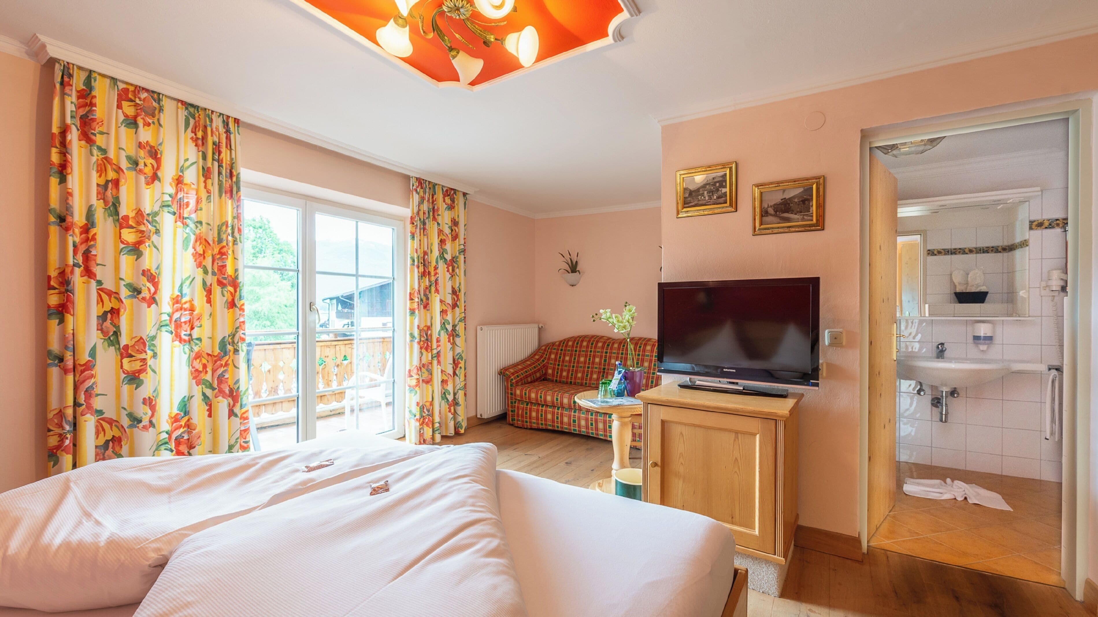 Een slaapkamer met een bed, een televisie, een bank en een badkamer zichtbaar door een open deur.