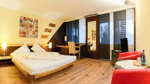 A hotel room with a bed, desk, chair, TV, and a red sofa.