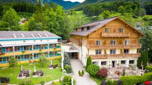A traditional wooden building with a balcony, surrounded by lush greenery and a mountainous backdrop.