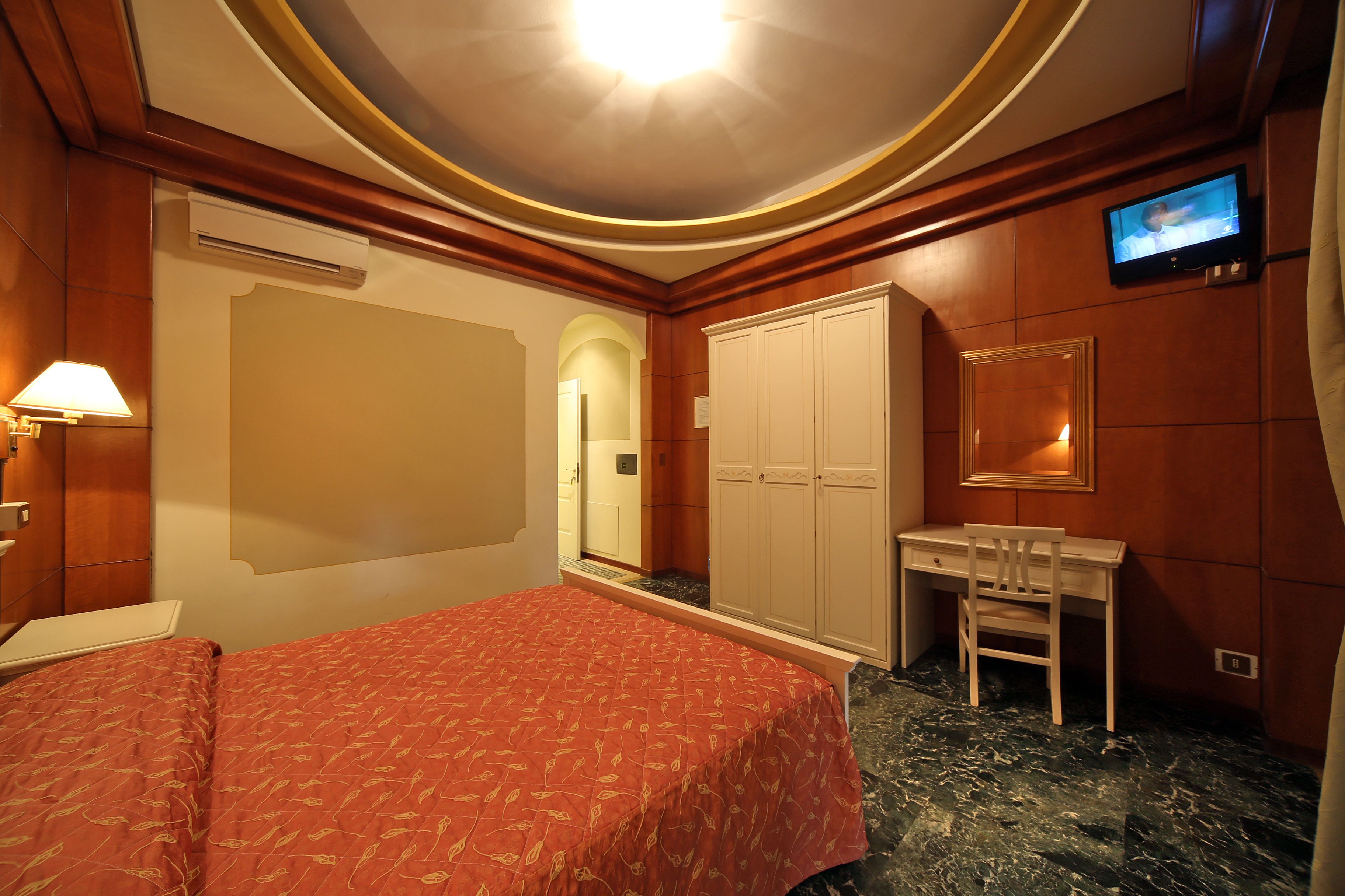 Una habitación de hotel con cama, escritorio, silla, televisión y armario.