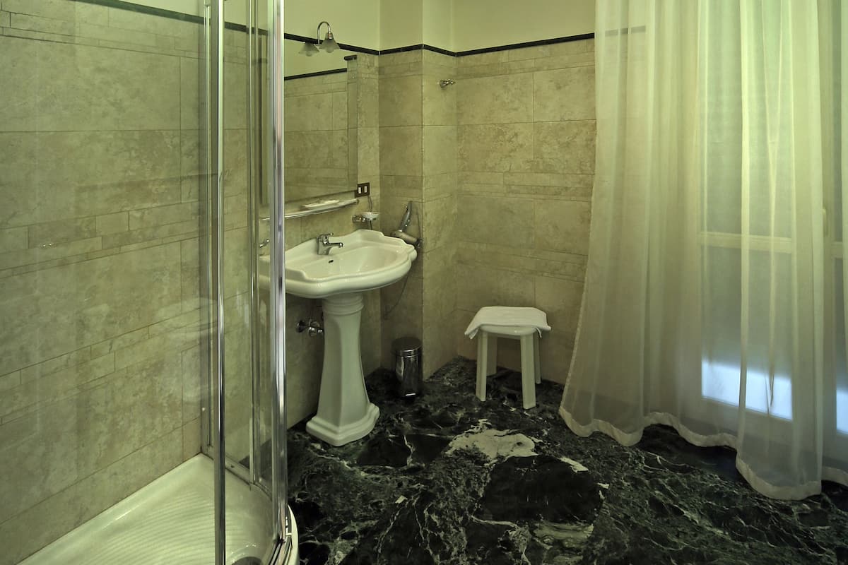 A bathroom with a glass-enclosed shower, a pedestal sink, and a marble floor.