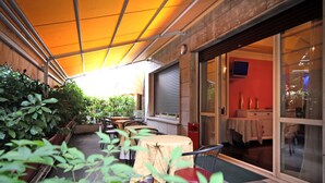 An outdoor seating area with tables and chairs, a covered walkway, and a glass door leading to an interior space. - Bed and Breakfast La Terrazza (Brescia)