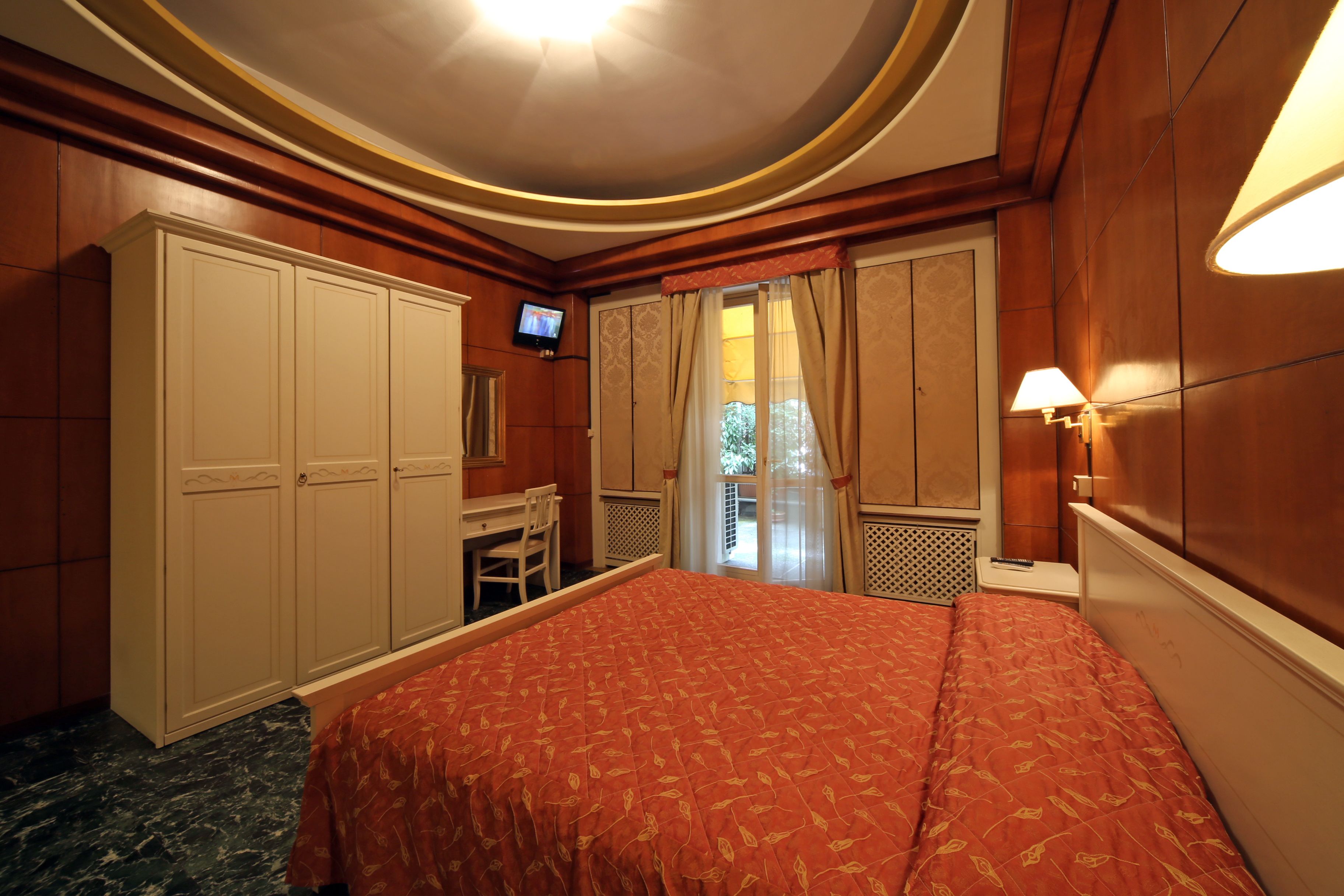 Une chambre d’hôtel avec un lit, un bureau, une télévision et une fenêtre avec des rideaux.