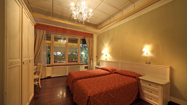 A bedroom with two beds, a chandelier, a window with curtains, and a nightstand. - Bed and Breakfast La Terrazza (Brescia)