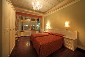A bedroom with two beds, a chandelier, a window with curtains, and a nightstand. - Bed and Breakfast La Terrazza (Brescia)