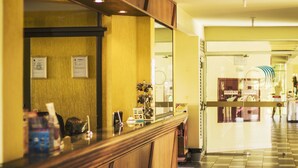 A reception area with a wooden counter, a mirror, and a wall with framed notices. - Canzi Cataratas Hotel (Foz do Iguacu)
