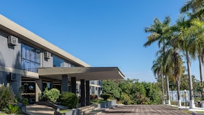 A modern hotel with a covered entrance, paved driveway, and landscaped garden with palm trees. - Canzi Cataratas Hotel (Foz do Iguacu)