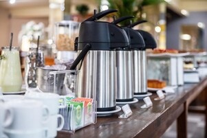 Montaje de bufé con varias máquinas de café de acero inoxidable y una variedad de alimentos.