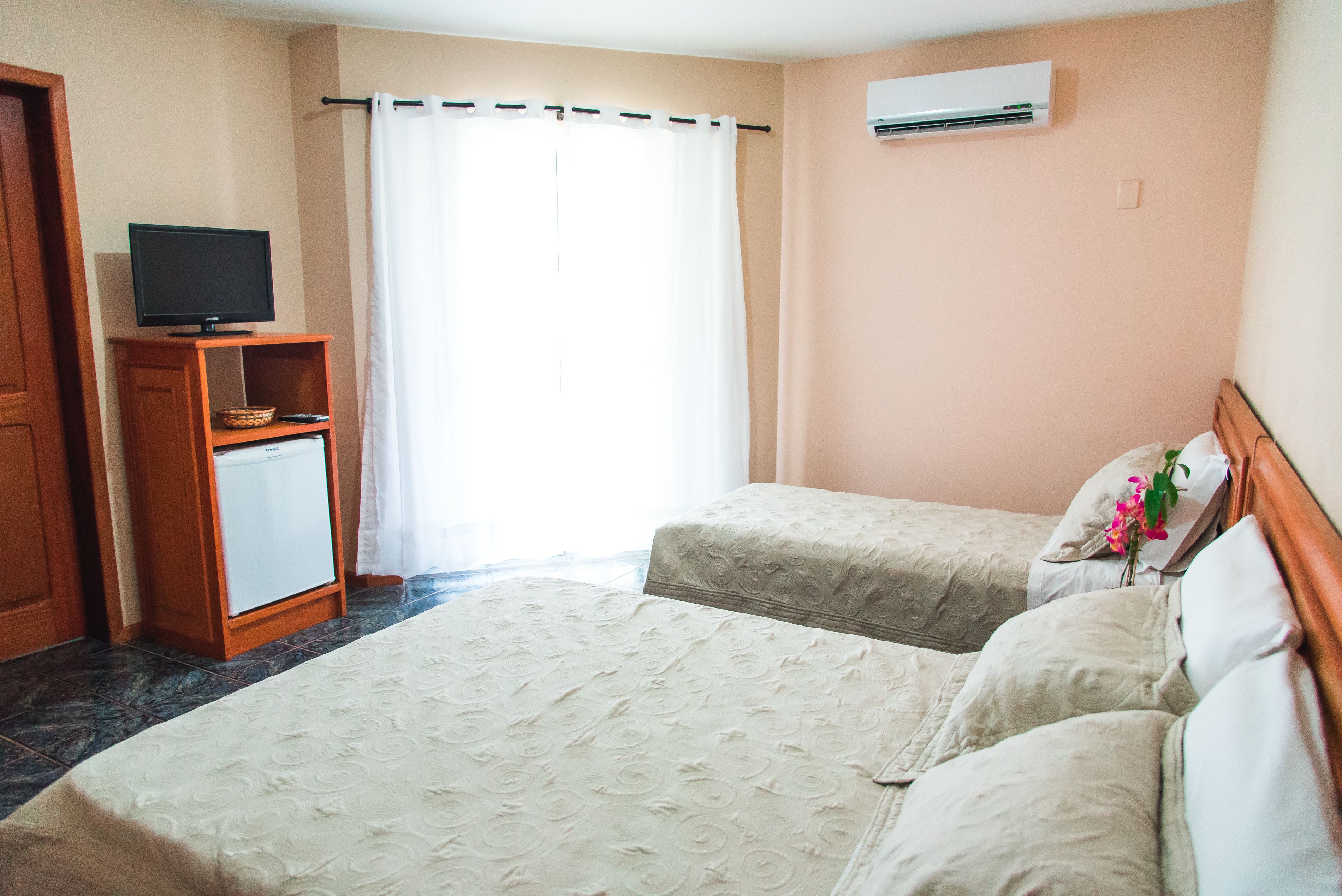 Habitación de hotel con dos camas, un televisor sobre un mueble de madera y un aire acondicionado en la pared.