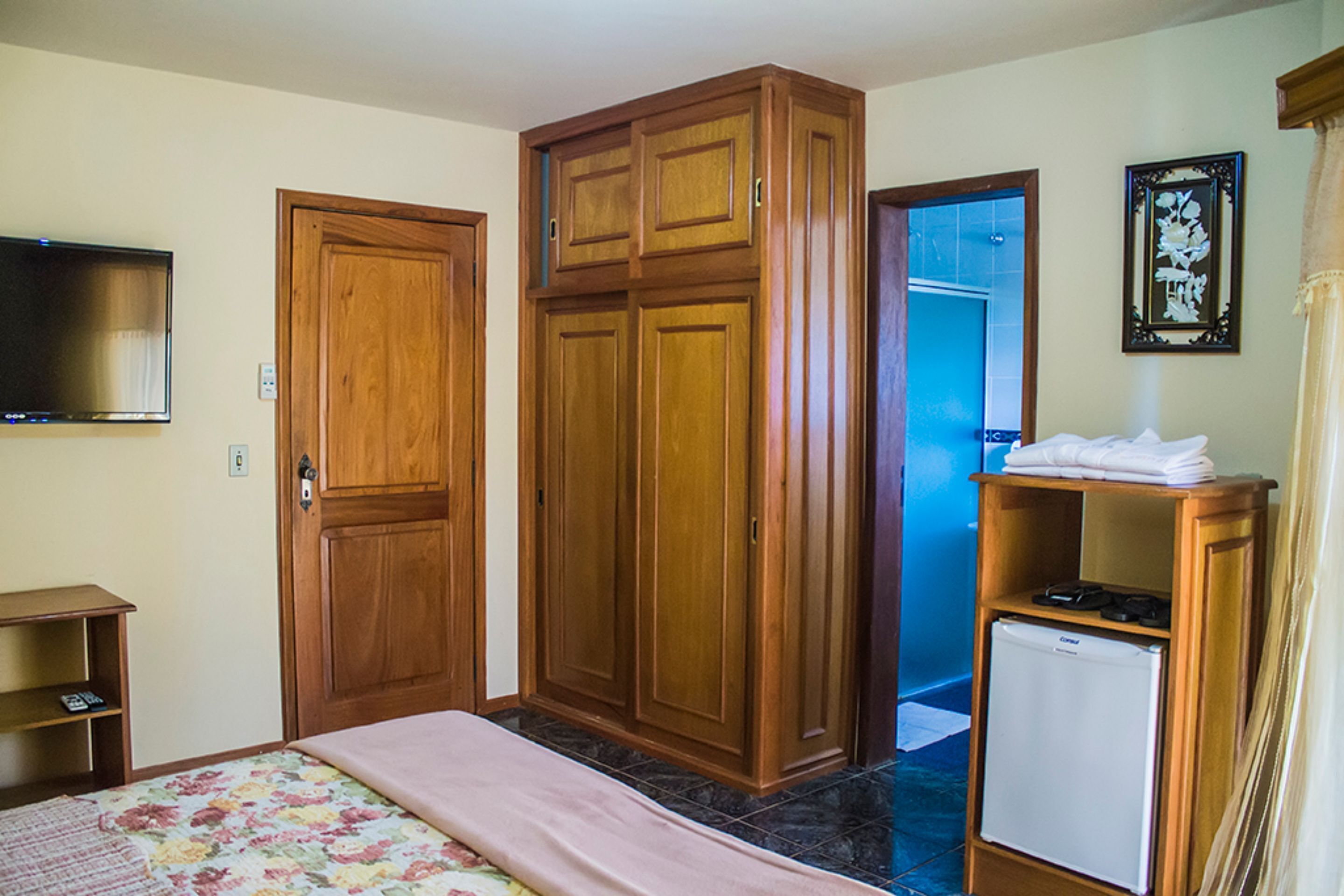 Un dormitorio con cama, armario de madera, refrigerador pequeño y televisor en la pared.