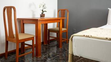 A room with a wooden table and two chairs, a bed with a white bedspread, and a small potted orchid on the table.