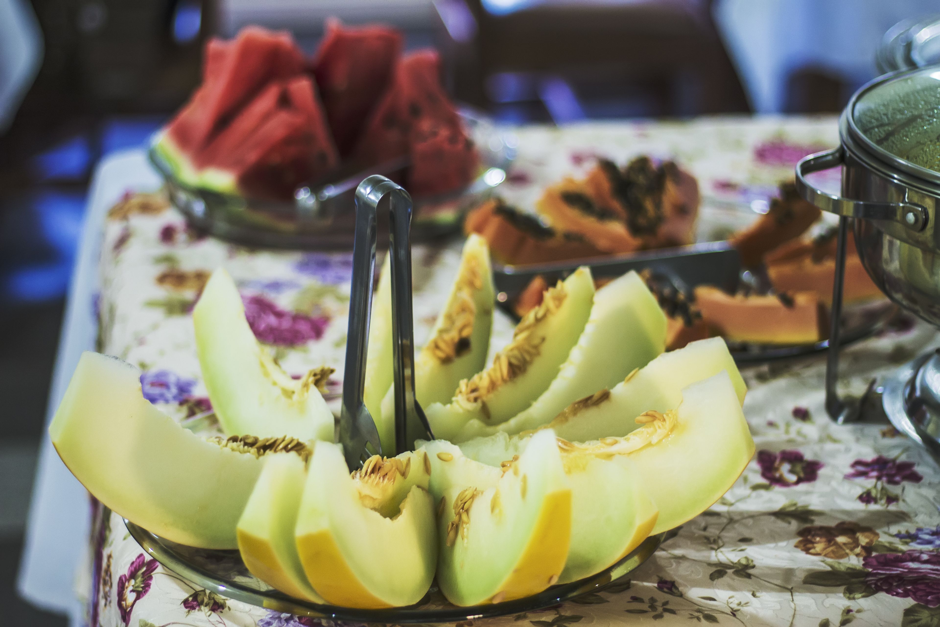 Ein Tisch mit einer blumigen Tischdecke, ein Teller mit geschnittenem Cantaloupe und eine Schüssel Wassermelone.