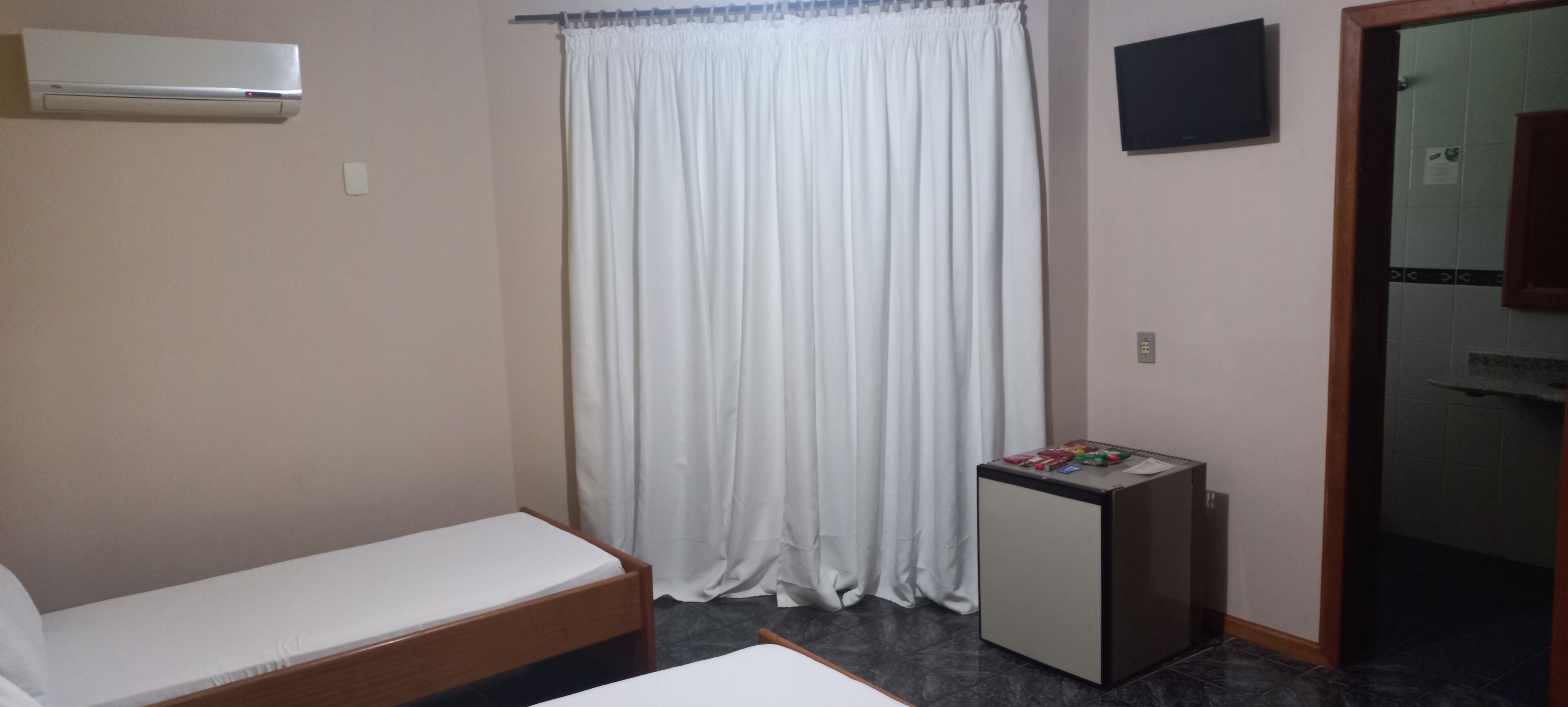 A small room with a bed, a desk, a white curtain, and a wall-mounted air conditioner.