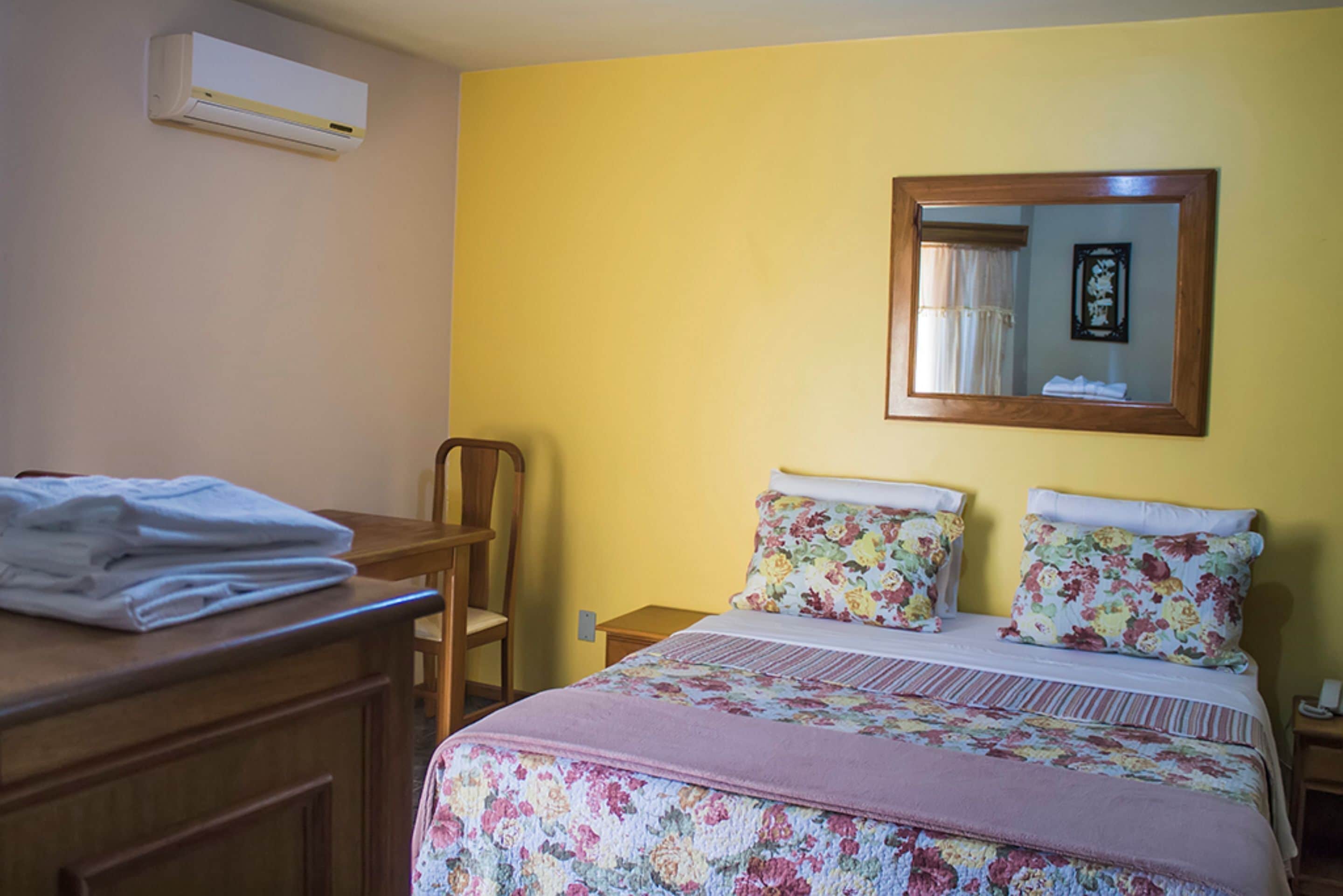 Un dormitorio con una cama, una silla, una mesita de noche y un equipo de aire acondicionado.