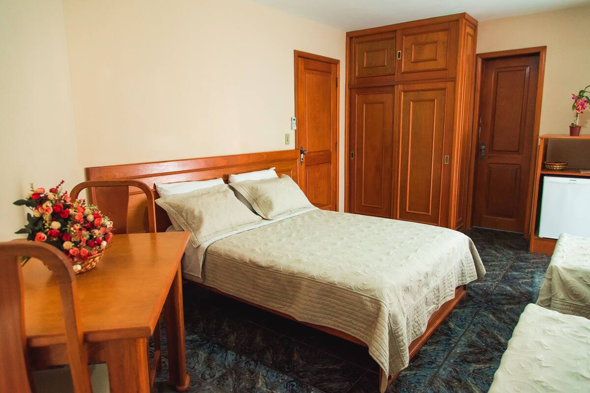 A hotel room with a bed, a wooden desk, a chair, and a large wardrobe.