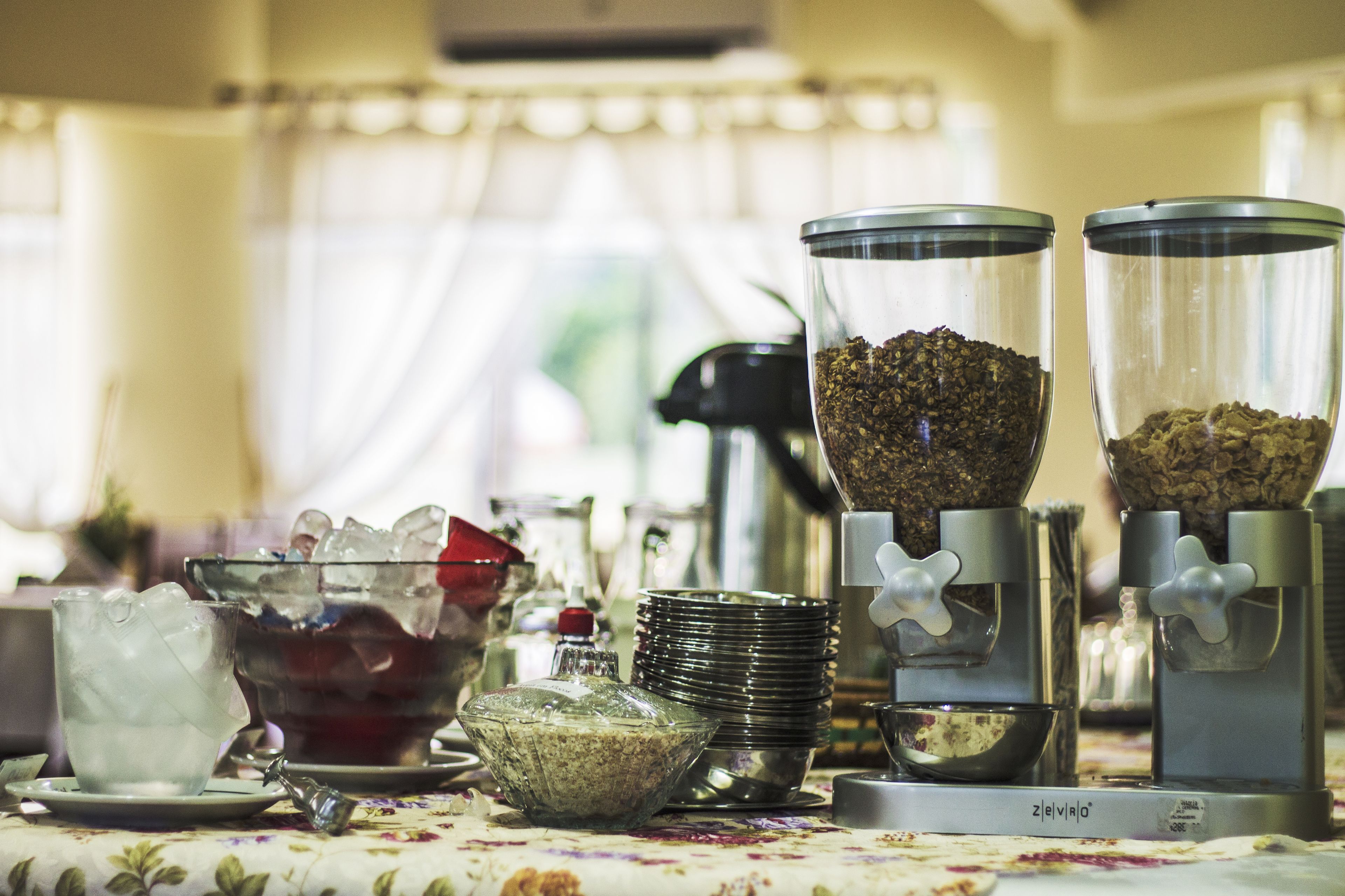 A breakfast buffet setup with various food dispensers, bowls, and plates on a table.