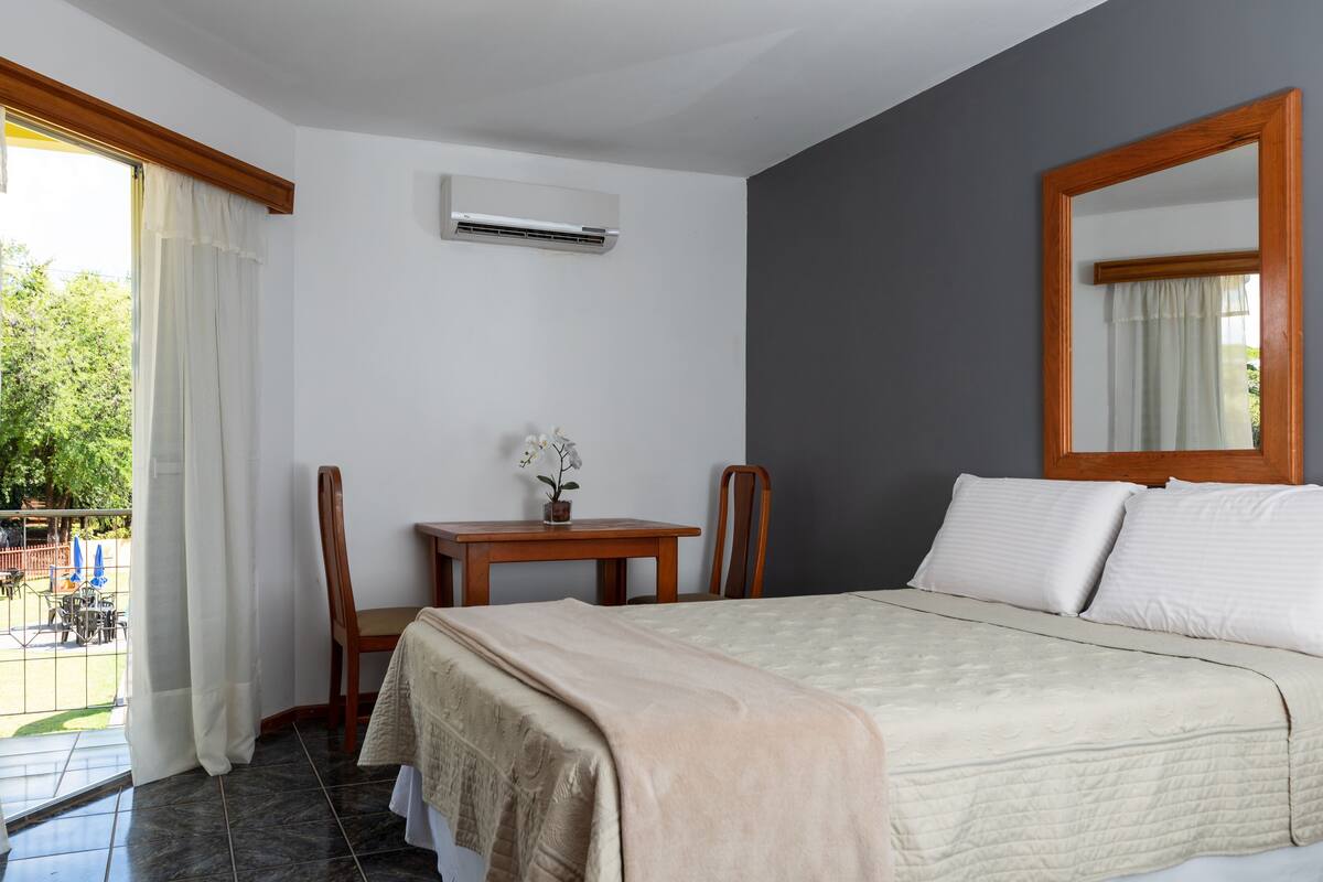 A bedroom with a bed, a desk, a chair, and a window with curtains.