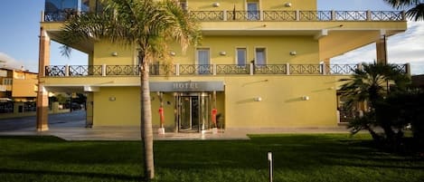 Un hotel de dos pisos con fachada amarilla, un balcón en el nivel superior y una puerta giratoria en la entrada.