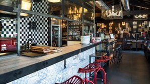 Una zona de bar con un revoque de baldosas a cuadros, una barra de madera y taburetes rojos.