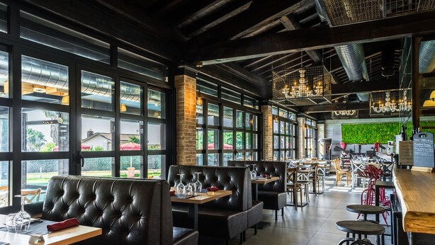 Interior de un restaurante con cabinas de cuero, mesas de madera y grandes ventanales con vistas al exterior.