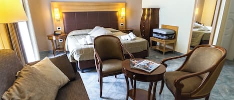 A hotel room with a bed, two armchairs, a small table, a nightstand, and a mirror.