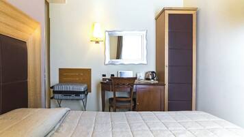 Habitación de hotel con cama, escritorio, silla, armario y espejo en la pared.