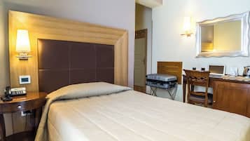 A hotel room with a large bed, a desk with a computer, a chair, a lamp, and a mirror.