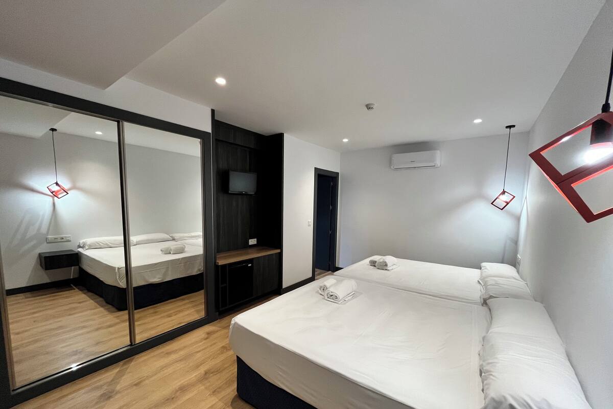 Habitació d'hotel moderna amb un llit gran, un mirall, una televisió i una petita taula de treball.