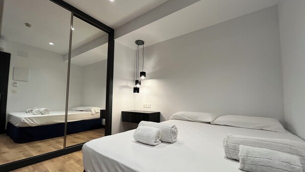 A modern hotel room with a large mirror, a bed with white linens, a bedside table, and a wall-mounted light fixture. - New "Villa Albero" Boutique (Torremolinos)