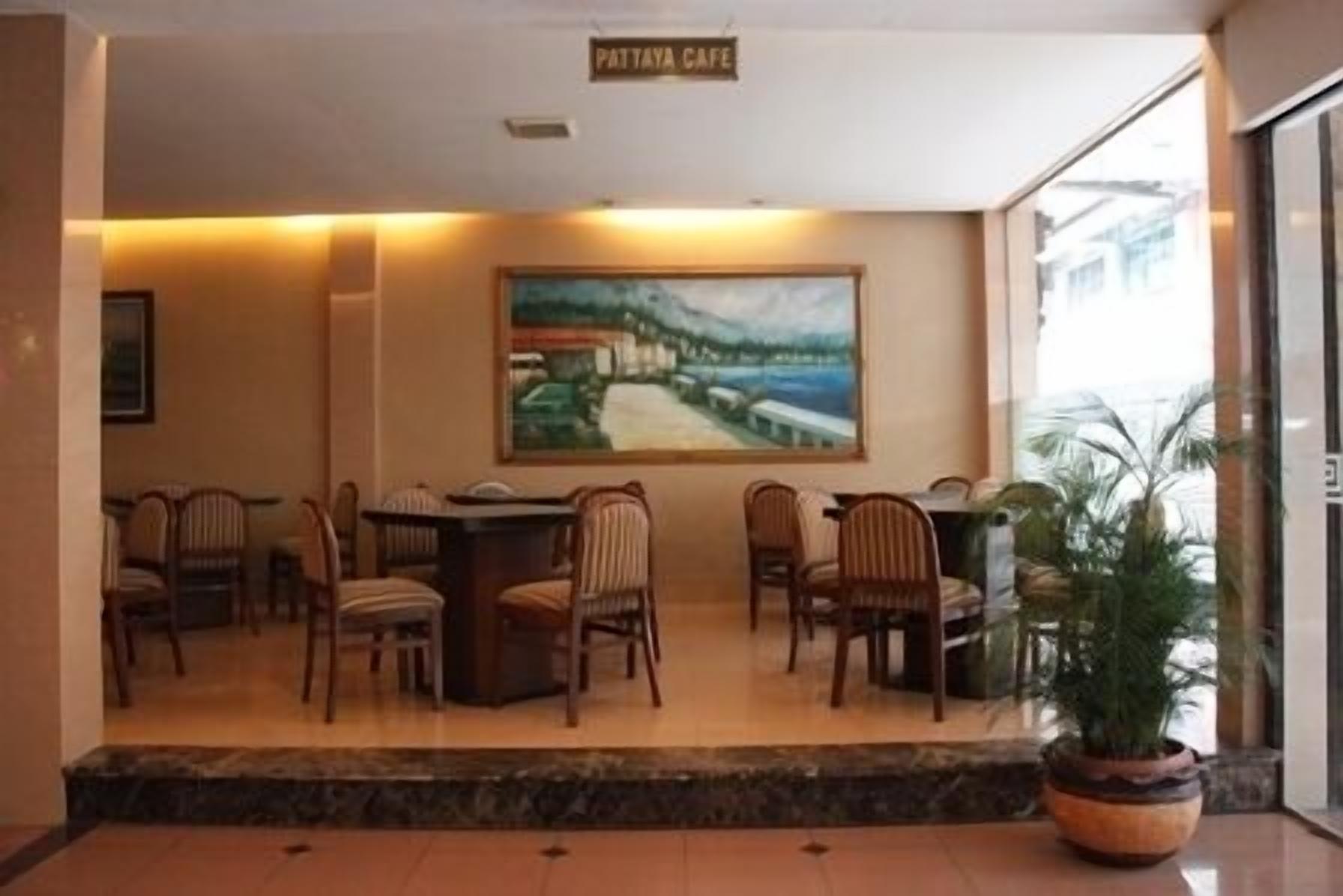 A lobby with a reception desk, several chairs, a large painting, and a sign that reads "PATTAYA CAFE".