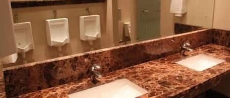 A bathroom with two sinks, a marble countertop, and three urinals.