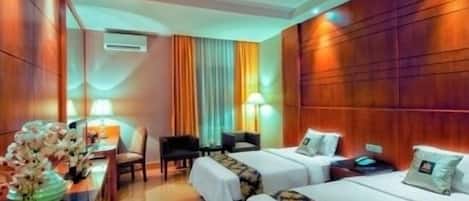 A hotel room with two beds, a desk with a chair, a small table with a vase of flowers, and a wall-mounted air conditioner.