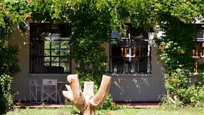 A building with a garden area featuring a unique sculpture, a seating area with chairs, and a window with a view of greenery. - Hotel Tafi (Tafi del Valle)